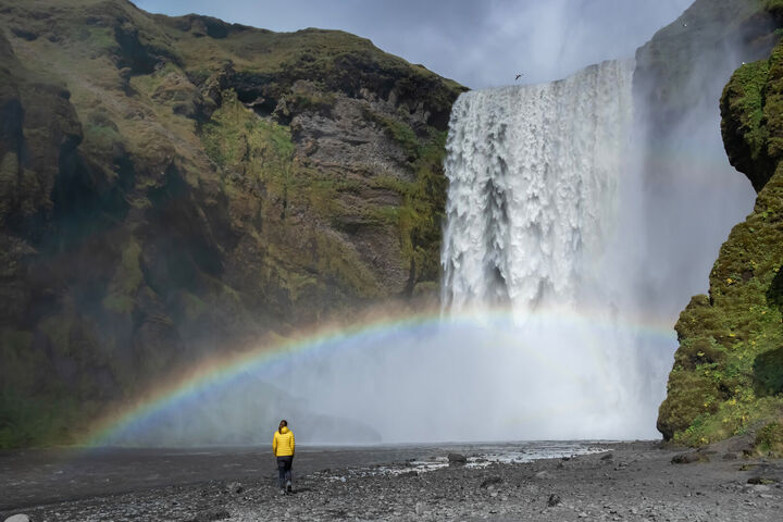 Skógafoss Wasserfall in Island mit einem Regenbogen, umgeben von üppiger Landschaft und klarem Himmel